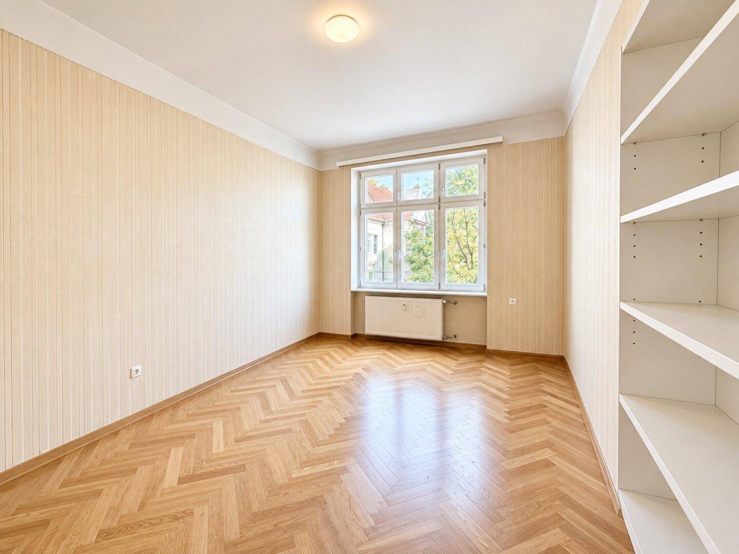 Leerer Raum mit Fischgrätparkett, gestreiften Tapeten und einem großen Fenster, bietet viel Gestaltungspotenzial.