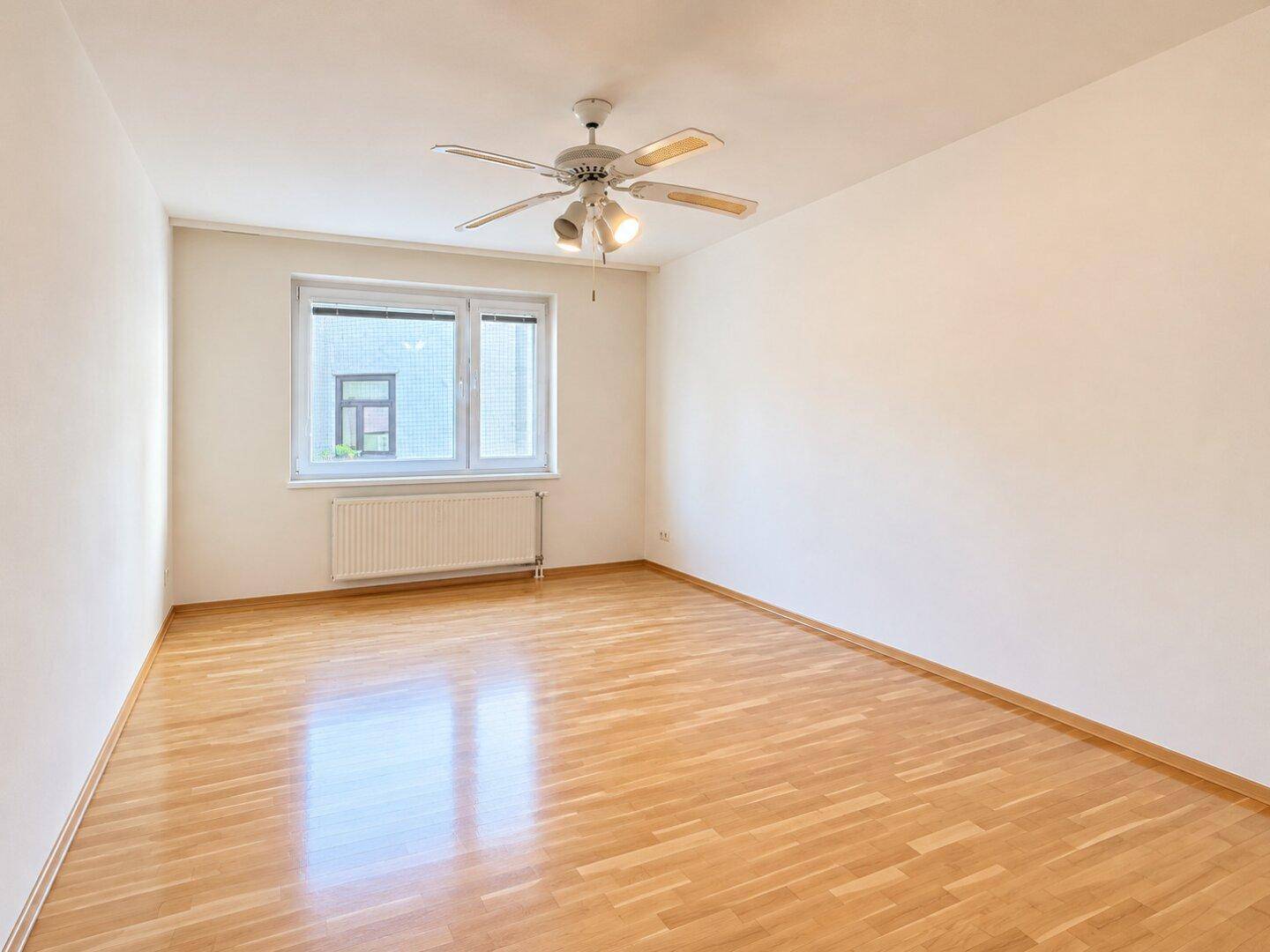 Leeres Schlafzimmer mit Holzboden, Deckenventilator und großem Fenster.
