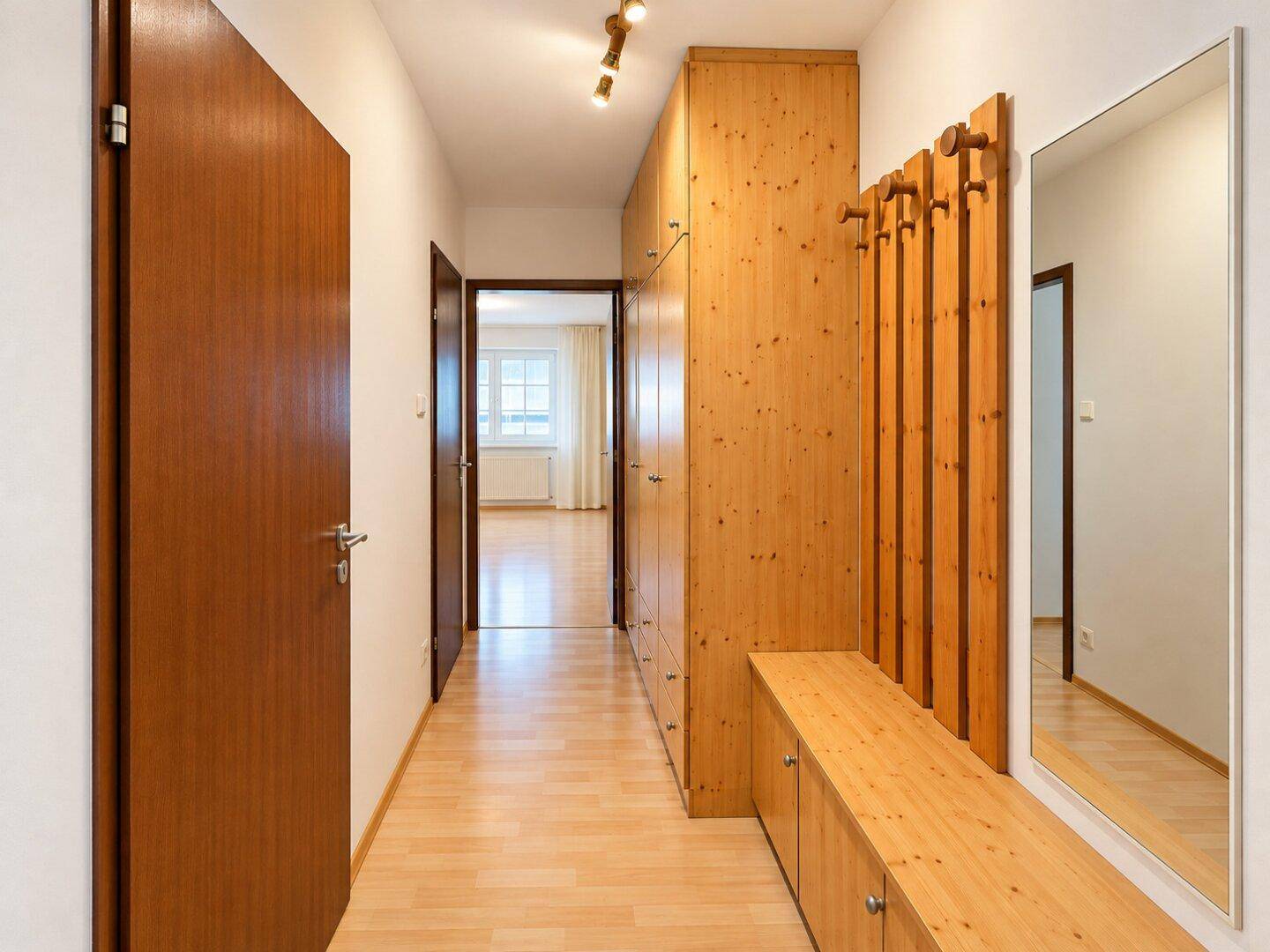 Flur mit Holzboden, Einbauschränken und Garderobe mit Spiegel.
