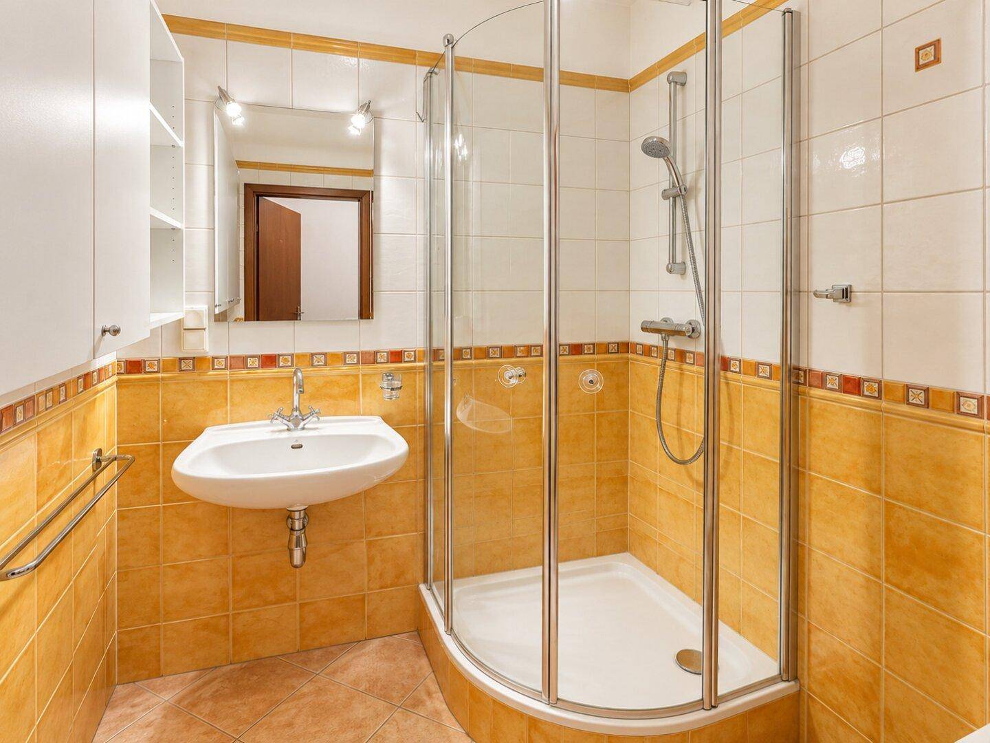 Badezimmer mit gelben Fliesen, Duschkabine, Waschbecken und Spiegelschrank.