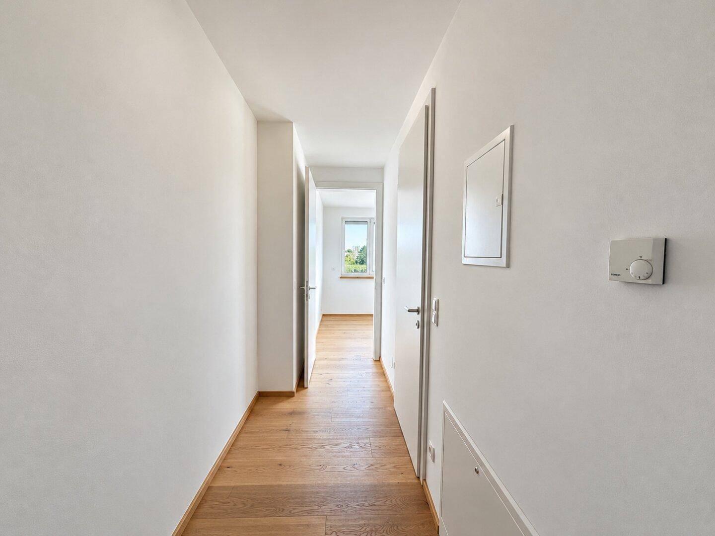 Heller Flur mit Holzboden, weißen Wänden und Zugang zu weiteren Räumen.