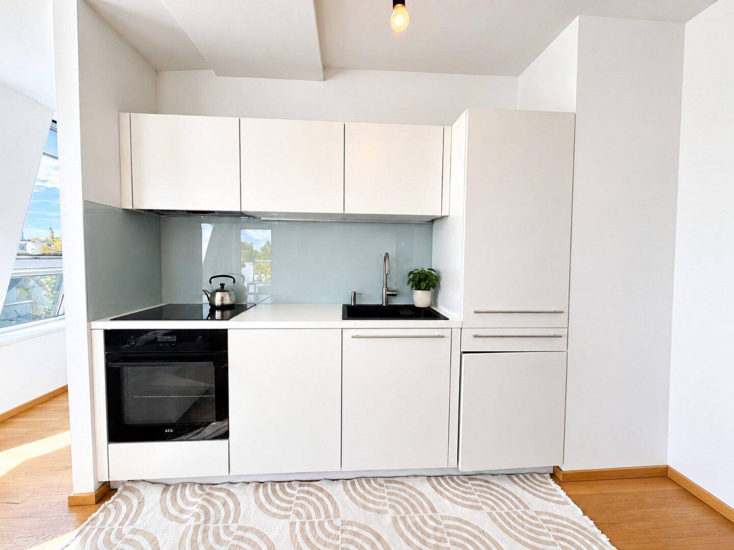 Kompakte, moderne Küchenzeile mit weißen Schränken, Induktionskochfeld und Backofen.