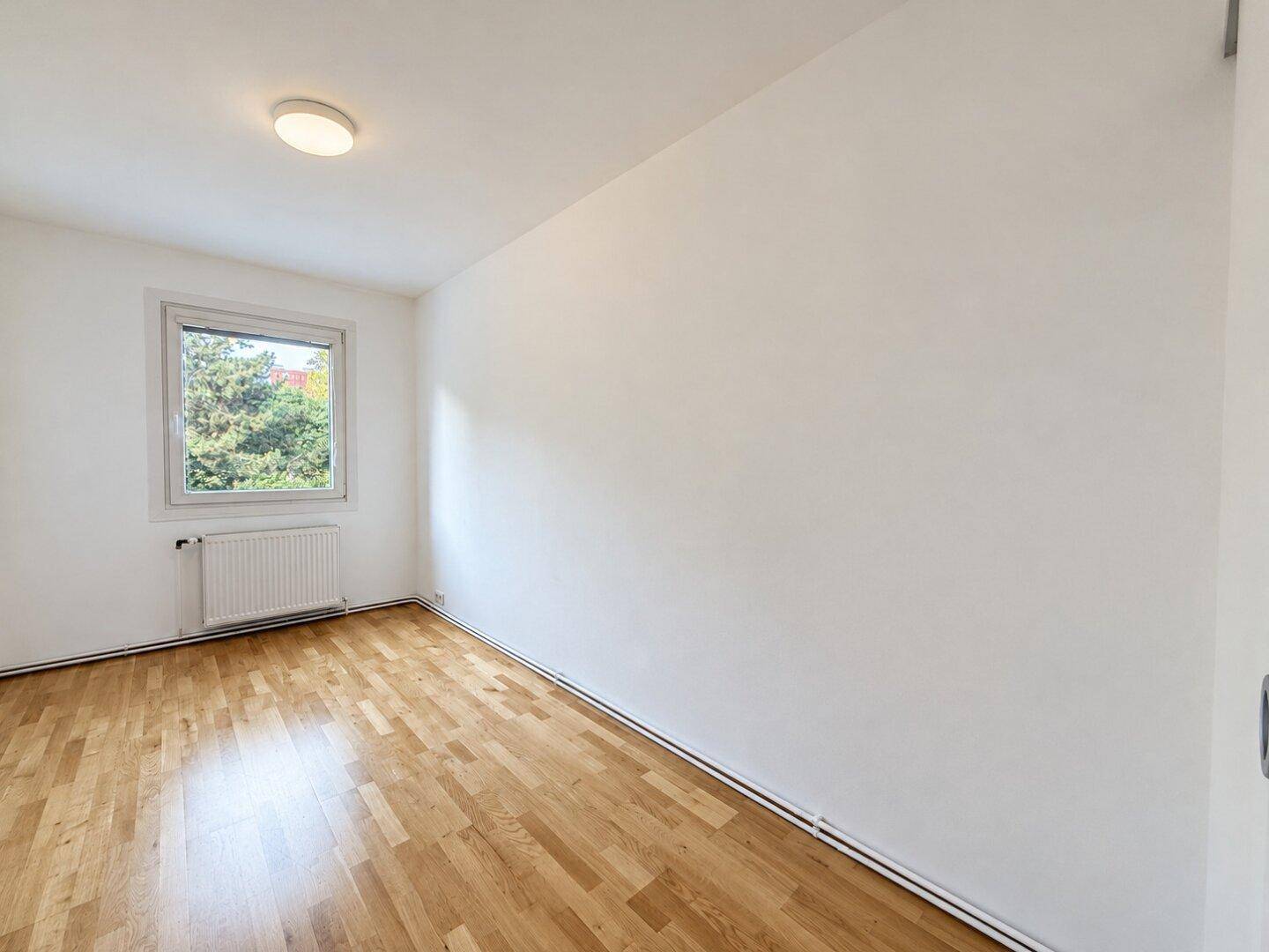 Kleiner, heller Raum mit Parkettboden und Fenster, geeignet als Schlafzimmer oder Arbeitszimmer.