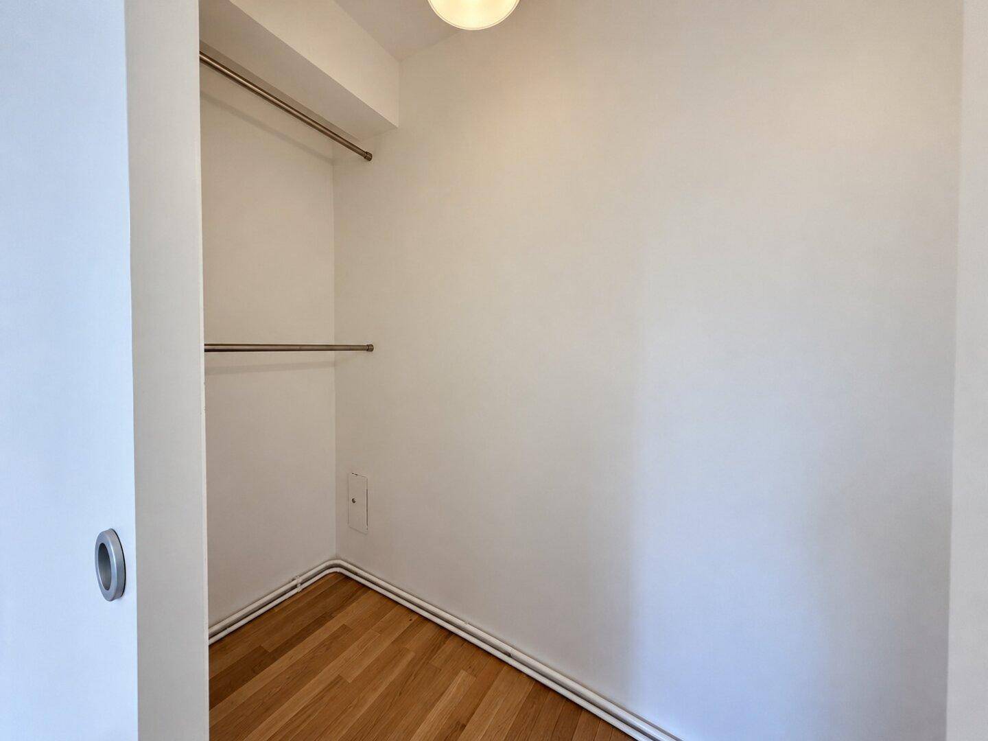 Praktischer begehbarer Kleiderschrank mit Kleiderstangen und Holzfußboden, bietet viel Stauraum.