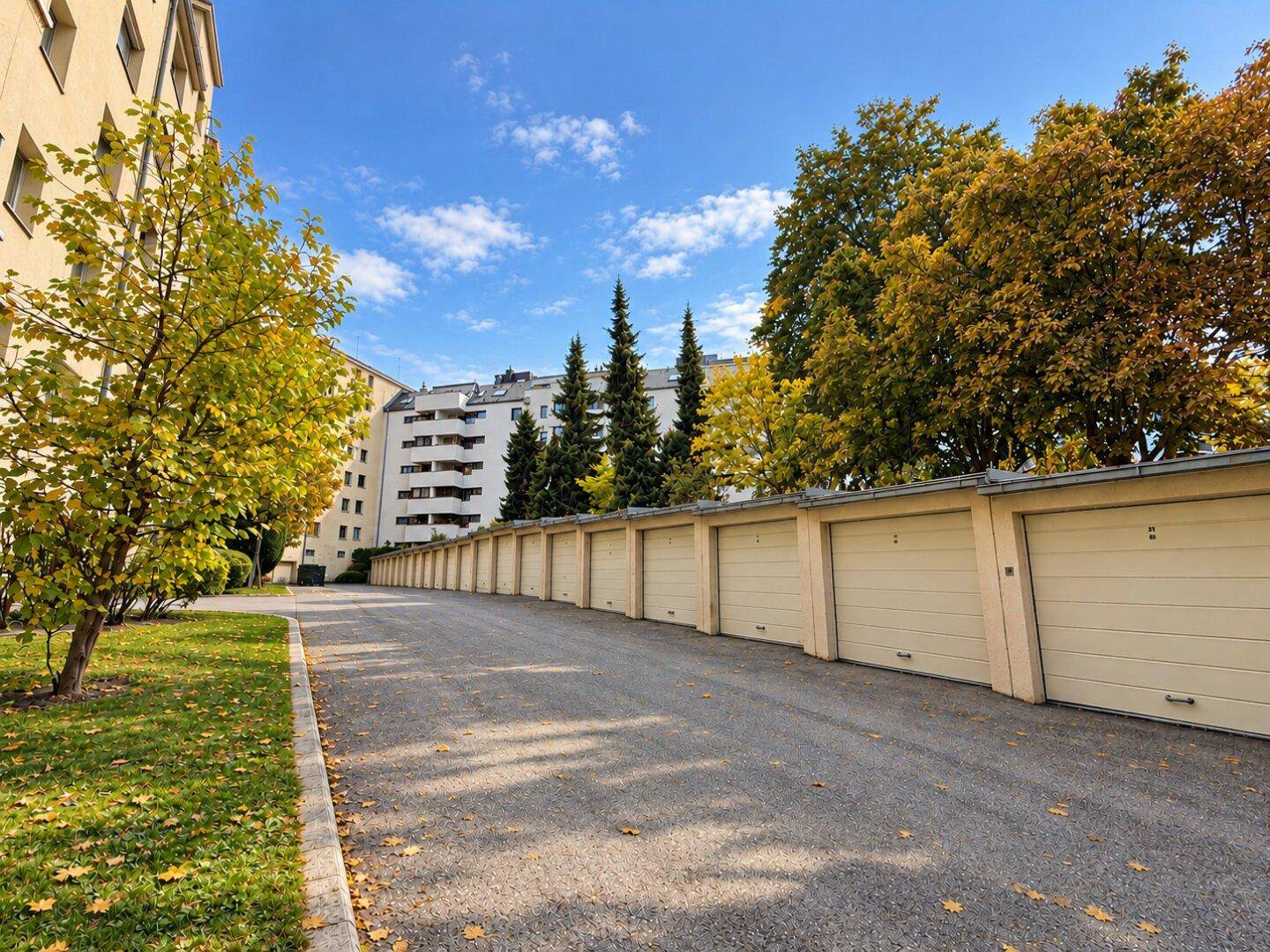 Reihe von Garagen mit Zufahrt und Bäumen im Herbstlaub vor einem Wohngebäude.