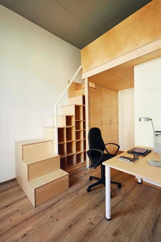 Helles Studentenzimmer mit Schreibtisch, Holztreppe und Hochbett auf einer Galerie.