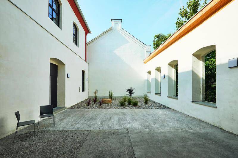 Kleiner, gepflasterter Innenhof zwischen weißen Gebäuden mit minimalistischer Bepflanzung.