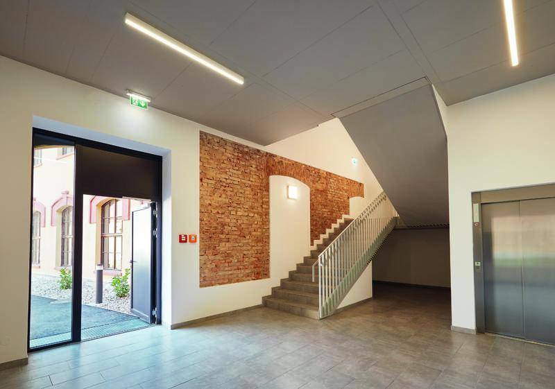 Moderner Eingangsbereich mit Treppenhaus, Aufzug und freigelegter Ziegelwand.