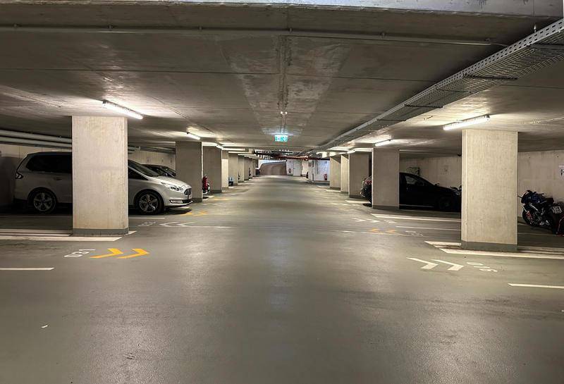 Geräumige Tiefgarage mit Betonpfeilern, geparkten Autos und heller Beleuchtung.