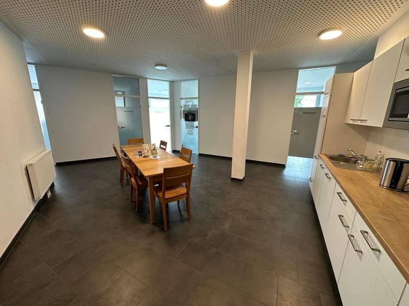 Heller Gemeinschaftsraum mit Küchenzeile, Holztisch und Blick auf angrenzende Büros.