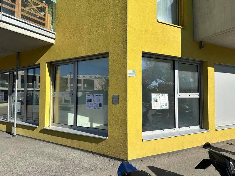 Nahaufnahme der gelben Fassade eines modernen Gebäudes mit großen Schaufenstern im Erdgeschoss.