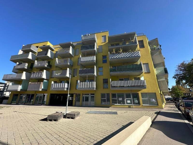 Auffälliges gelbes Wohngebäude mit zahlreichen Balkonen und Geschäften im Erdgeschoss.