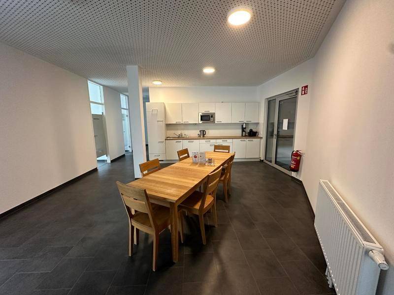 Geräumiger Gemeinschaftsbereich mit moderner Küche, Esstisch und dunklem Fliesenboden.