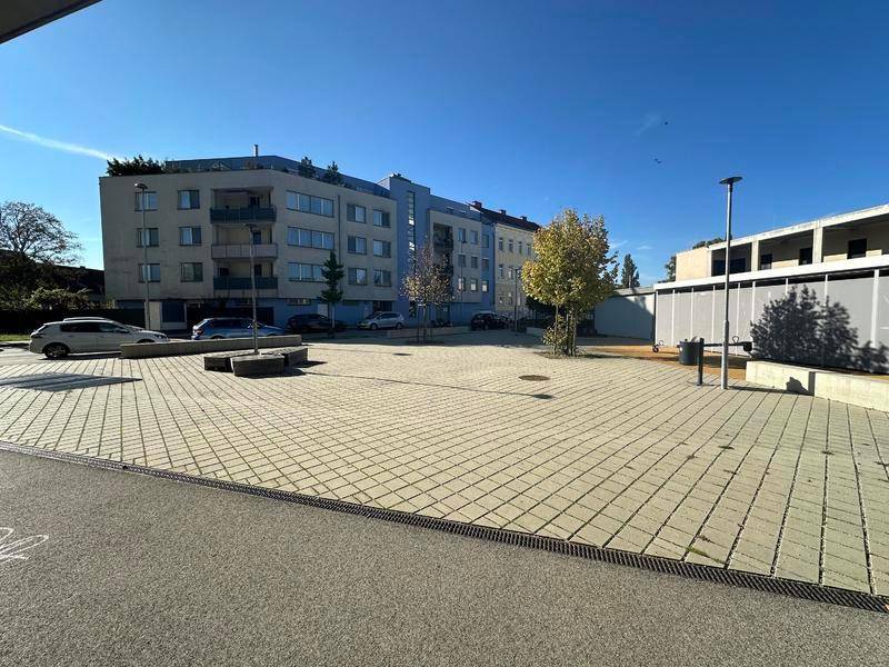 Außenansicht eines Wohngebäudes mit Parkplätzen und Bäumen unter blauem Himmel.