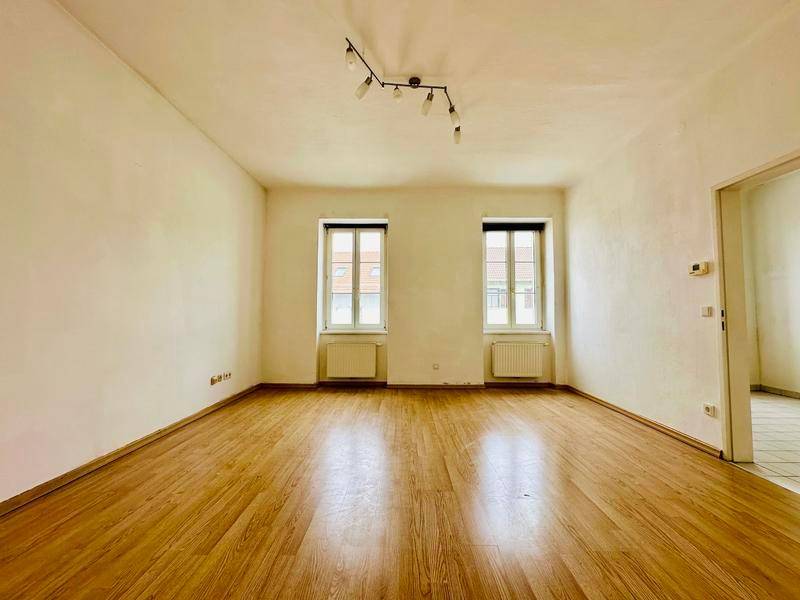 Heller, leerer Raum mit Laminatboden und zwei Fenstern, bereit zur individuellen Gestaltung.