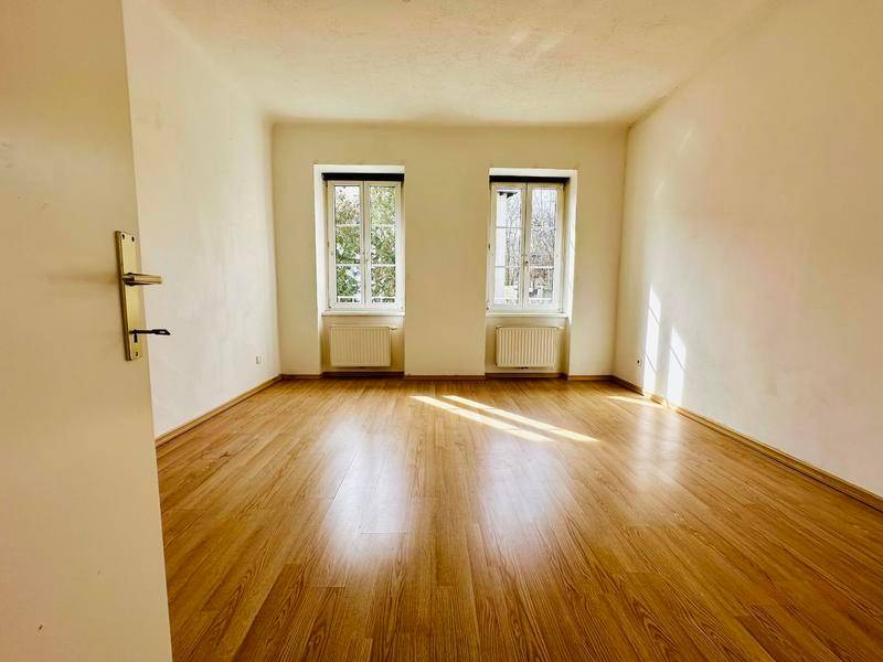 Sonniger, leerer Raum mit Laminatboden und zwei Fenstern, ideal für ein Wohn- oder Schlafzimmer.