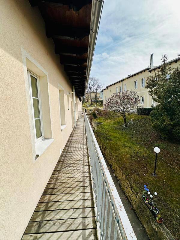 Langer Balkon entlang der Gebäudeseite mit Holzboden und Blick auf die grüne Umgebung.