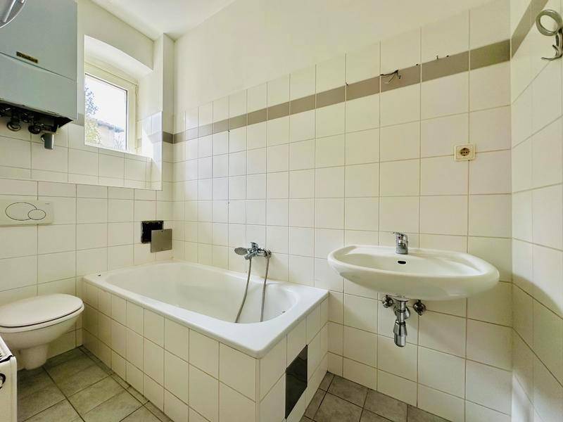 Funktionales Badezimmer mit Badewanne, WC, Waschbecken und weißen Wandfliesen im 80er-Jahre-Stil.