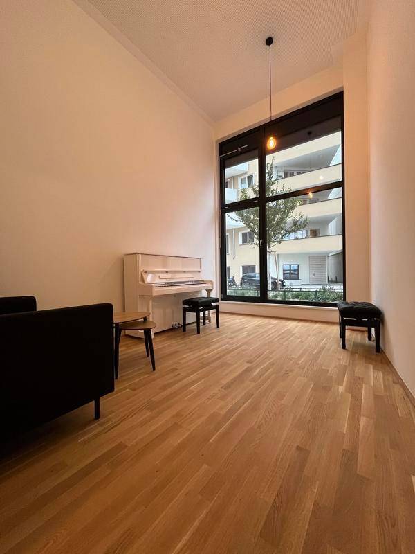 Geräumiger Wohnraum mit hohen Decken, einem eleganten Klavier und einem großen Fenster, das den Raum erhellt.