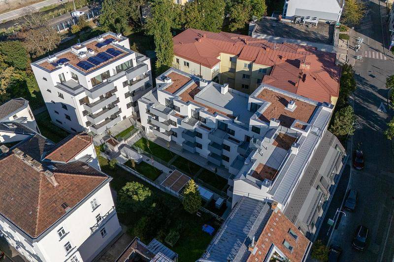 Luftaufnahme einer modernen Wohnanlage mit begrünten Innenhöfen und Solaranlagen auf dem Dach.