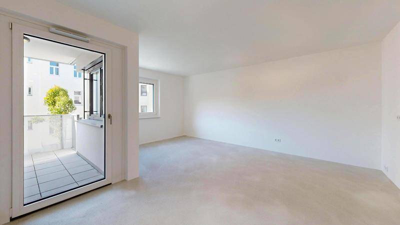 Geräumiger, unmöblierter Wohnbereich mit hellem Boden und Zugang zu einem Balkon.