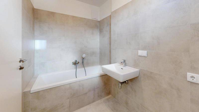 Modernes Badezimmer mit hellen Fliesen, eingebauter Badewanne und wandhängendem Waschbecken.