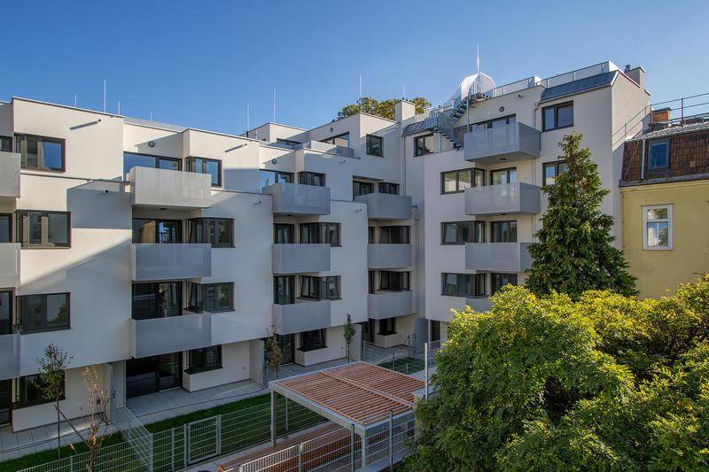 Zeitgenössische Wohngebäude mit Balkonen und einem begrünten Innenhof mit Bäumen.
