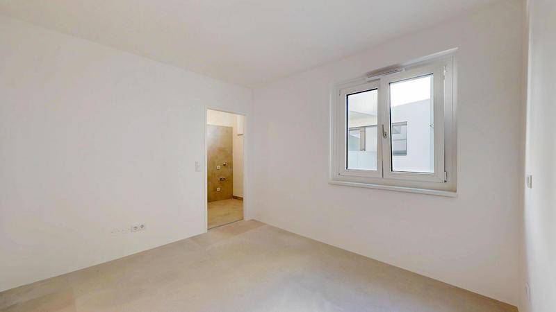 Heller, unmöblierter Raum mit Fenster und Zugang zu einem angrenzenden Badezimmer.