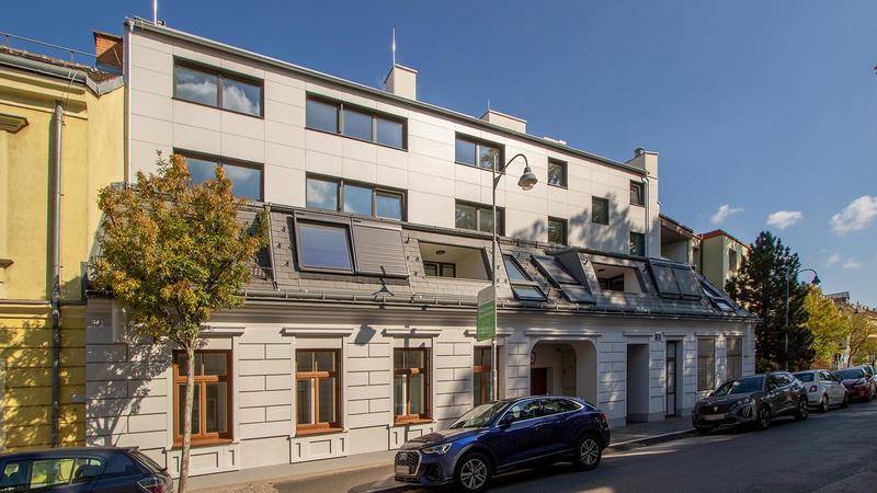 Fassade eines Wohngebäudes mit moderner Aufstockung und traditionellem Erdgeschoss an einer Straße.