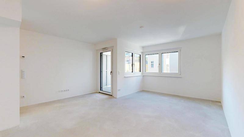 Unmöblierter Wohnbereich mit viel Tageslicht durch große Fenster und Balkontür.