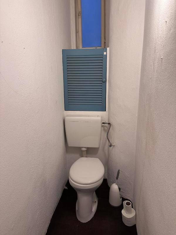 Separate Toilette mit Fenster und weißer Keramik, die eine Modernisierung benötigt.