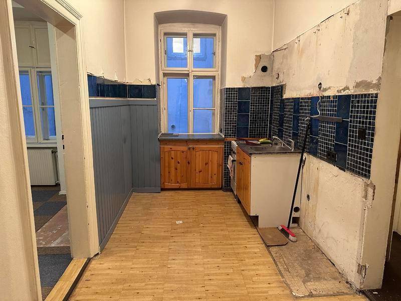 Küche in Renovierungszustand mit blauen Fliesen, Holzschränken und einem Fenster.