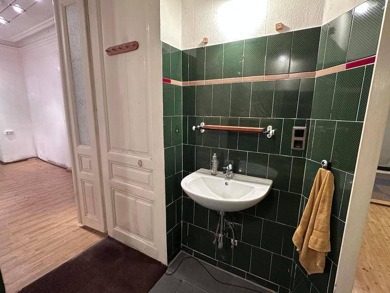 Badezimmer mit Waschbecken, grünen Fliesen und einer Tür, die in einen anderen Raum führt.