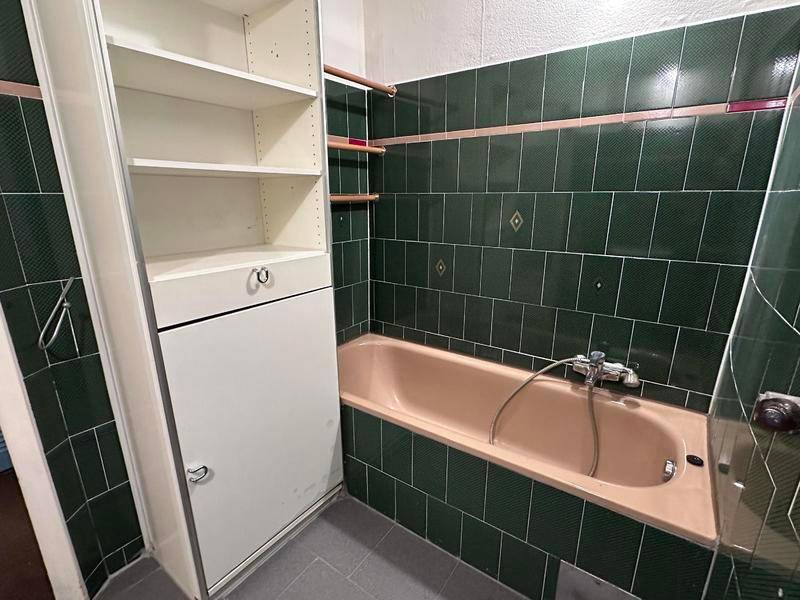 Badezimmer mit grünen Fliesen, einer Badewanne und einem Einbauschrank, das renoviert werden muss.