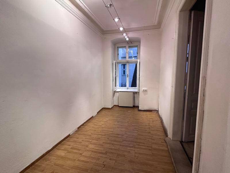 Heller Raum mit Holzboden, hohen Decken und einem geöffneten Fenster, das auf Renovierung wartet.
