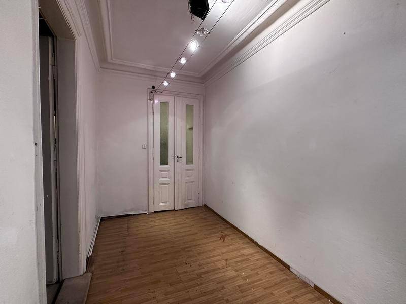 Langer, schmaler Raum mit Holzboden, hohen Decken und einer Doppeltür, die renoviert werden muss.
