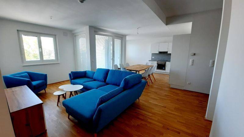 Geräumiger offener Wohn-Essbereich mit blauen Sofas, Holztisch und integrierter moderner Küche.