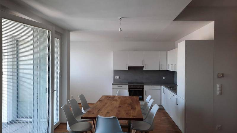Essbereich mit Holztisch und moderner weißer Küche, daneben eine große Schiebetür mit Jalousien.