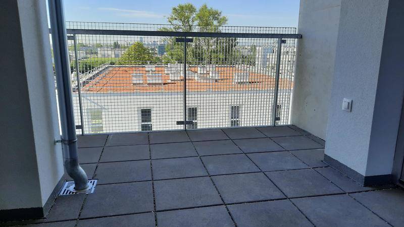 Geräumiger Balkon mit Fliesenboden und Metallgeländer, bietet einen Blick auf die umliegenden Gebäude.