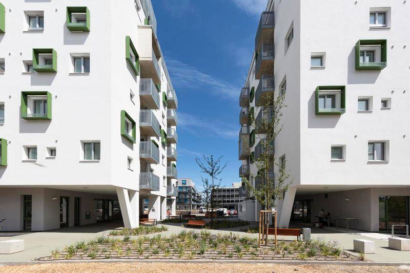 Moderne Wohngebäude mit weißer Fassade und grünen Akzenten, umgeben von einem begrünten Innenhof.