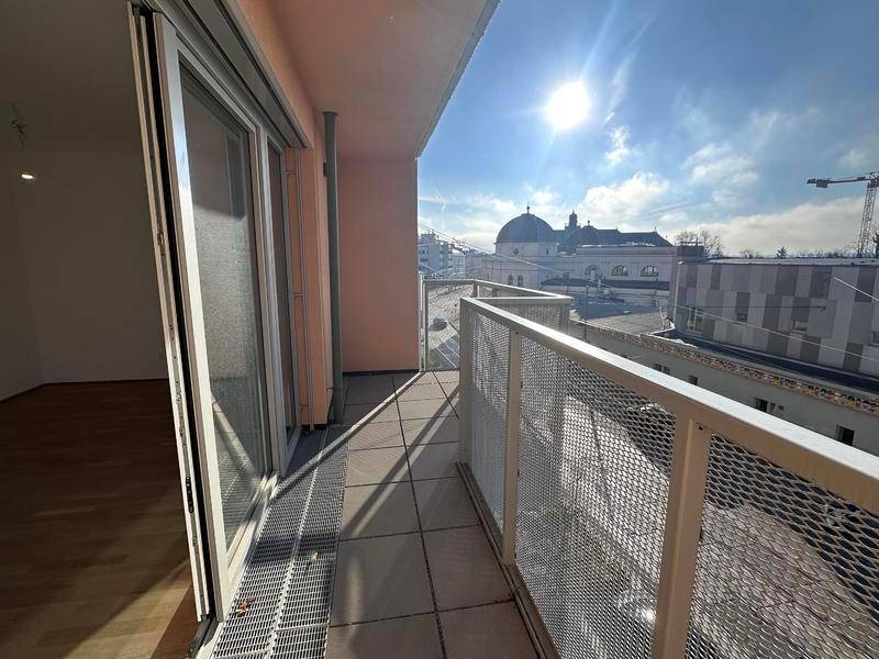 Sonniger Balkon mit Fliesenboden und Blick auf die Stadt und eine Kirche.