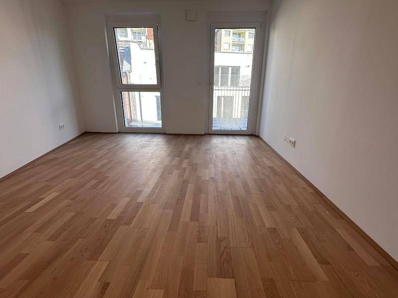 Helles Zimmer mit Parkettboden und großen Fenstern, die viel Tageslicht hereinlassen.
