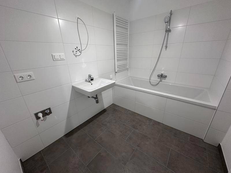 Helles Badezimmer mit Badewanne, Waschbecken und beheiztem Handtuchhalter.
