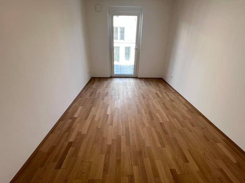 Leeres Zimmer mit Holzboden und einer Tür, die zu einem französischen Balkon führen könnte.