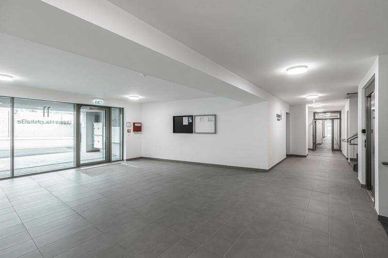Heller Eingangsbereich mit Fliesenboden und Zugang zu den Wohnungen in einem modernen Gebäude.