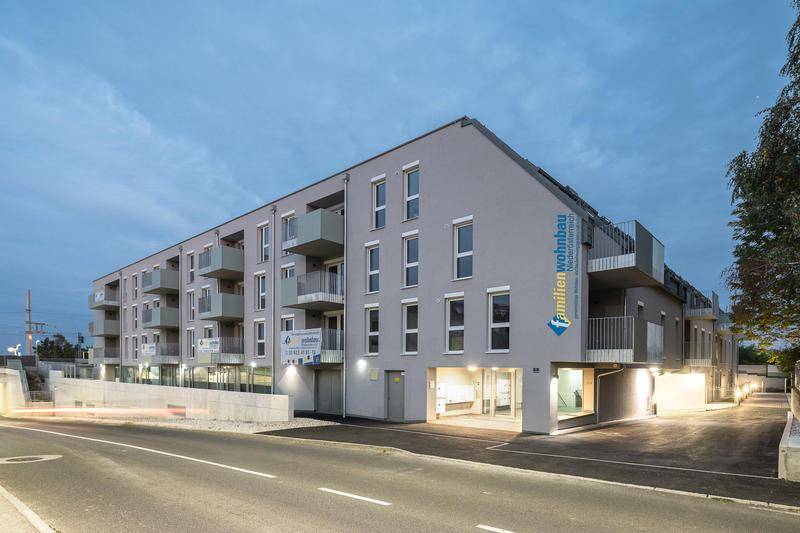 Moderne Wohnanlage bei Dämmerung mit beleuchteter Fassade und Balkonen.