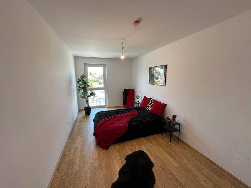 Schlafzimmer mit Holzboden, weißen Wänden, modernem Bett und einem Fenster für natürliches Licht.