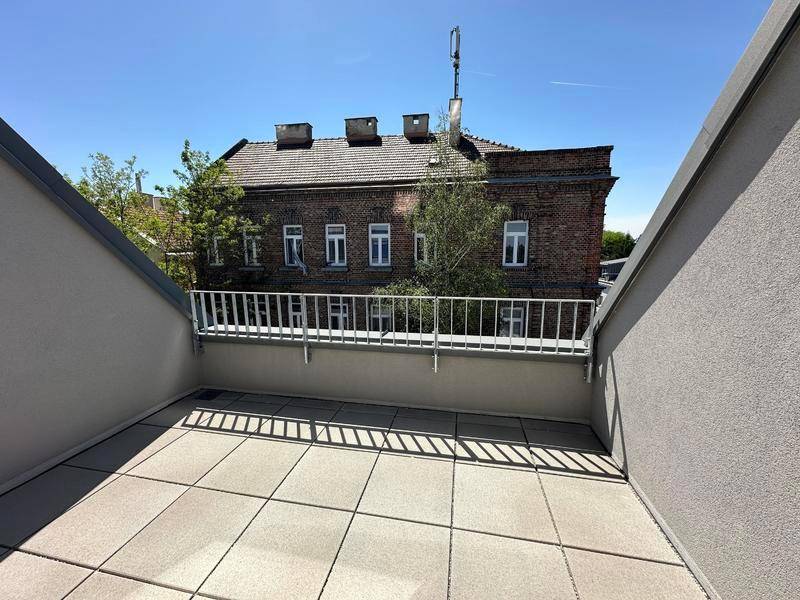 Geräumige Dachterrasse mit Fliesenboden und Blick auf ein charmantes Backsteingebäude gegenüber.
