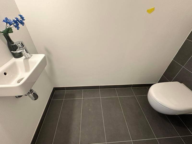 Gäste-WC mit dunkelgrauen Bodenfliesen, wandhängendem WC und einem kleinen Handwaschbecken.