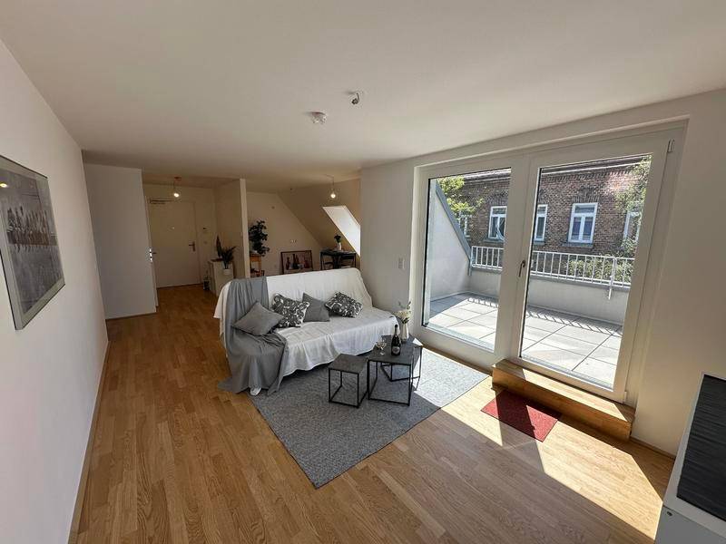 Lichtdurchfluteter Wohnbereich mit beigem Holzboden, modernem Sofa und direktem Zugang zur Außenterrasse.